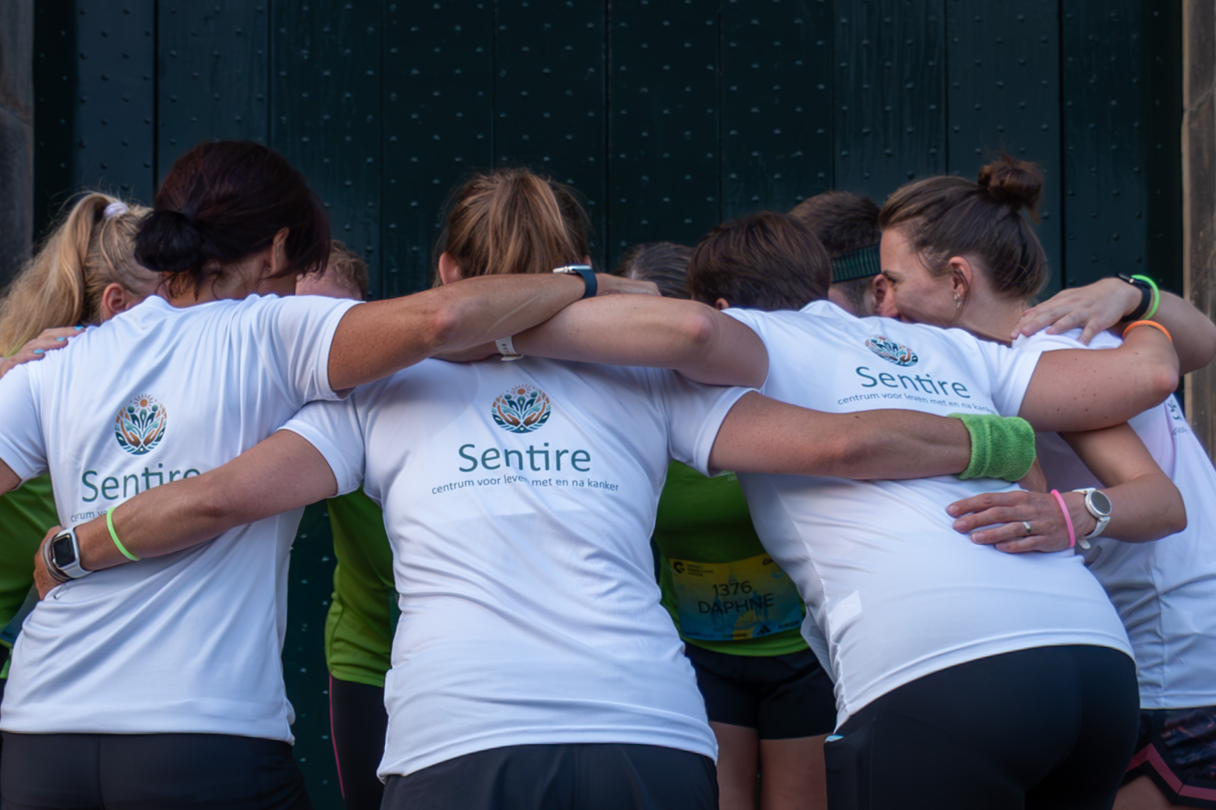 Groep deelnemers met Sentire-shirts in een sportieve omhelzing